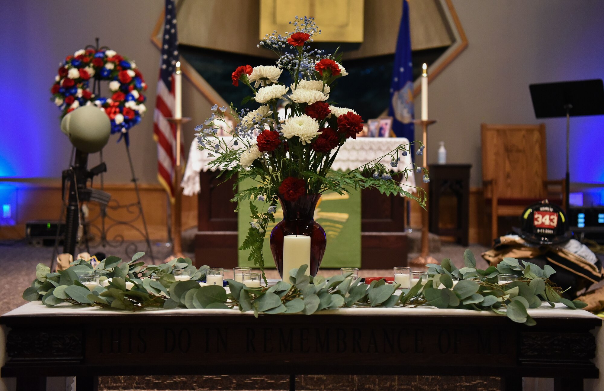 A table is decorated with a bouquet of red and white flowers, with candles and leaves.