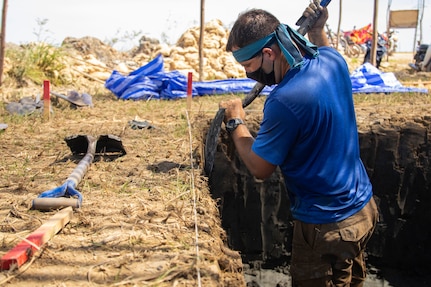 A man stands in a pit and shovels dirt.