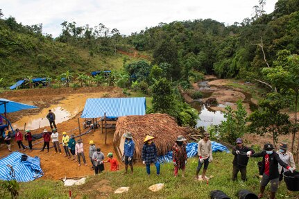 With a jungle in the background, people stand in a line as a bucket is passed from one person to another.