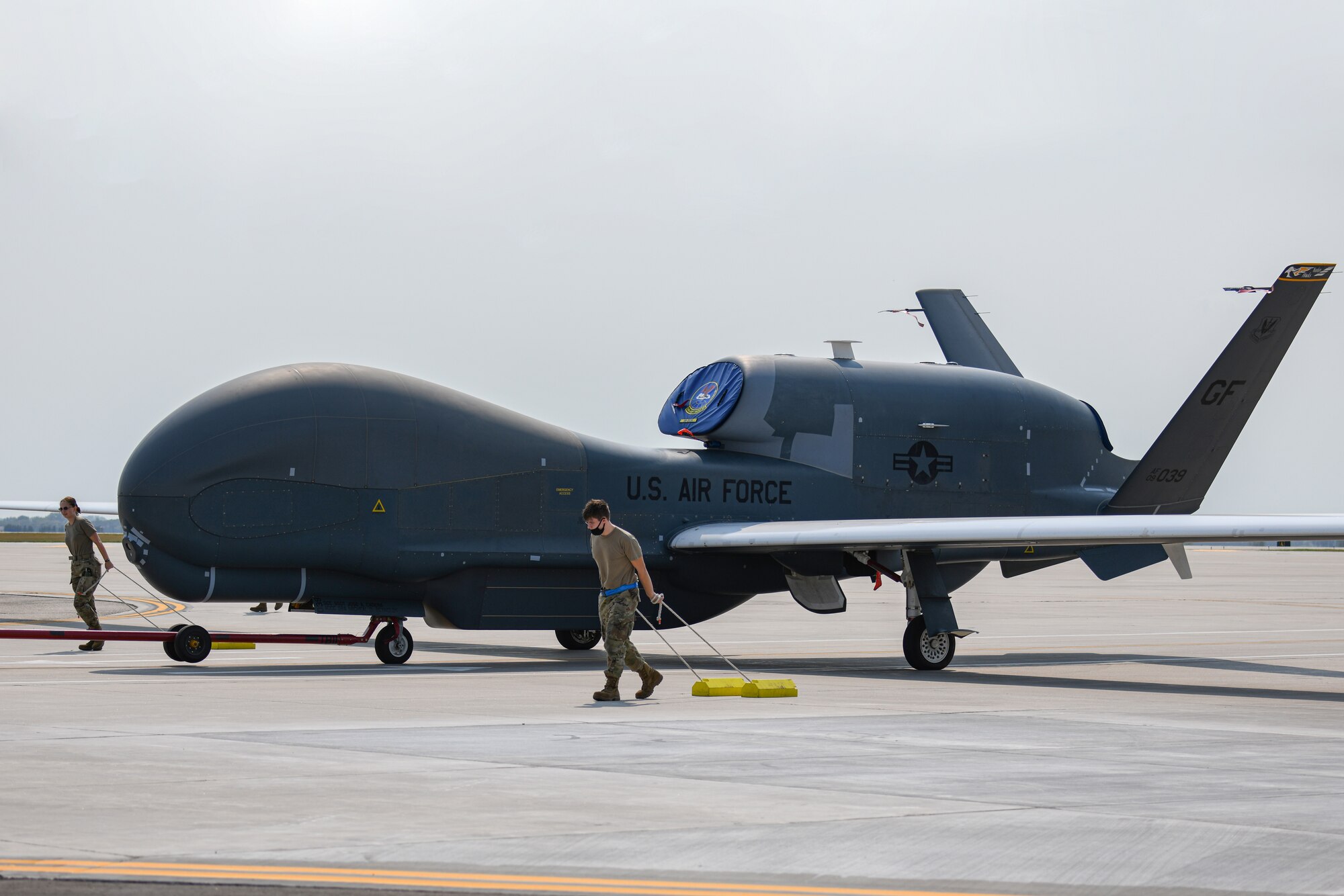 Crew chiefs assigned to the 319th Aircraft Maintenance Squadron, pull chocks beside an RQ-4 Global Hawk as it’s towed across the flight line during an exercise on Grand Forks Air Force Base, N.D., Aug. 19, 2021. The primary goal of this exercise was to accelerate change in the RQ-4 enterprise and to prove the Global Hawks can meet demands of the Agile Concept Employment concept for future operations. (U.S. Air Force photo by Airman 1st Class Ashley Richards)