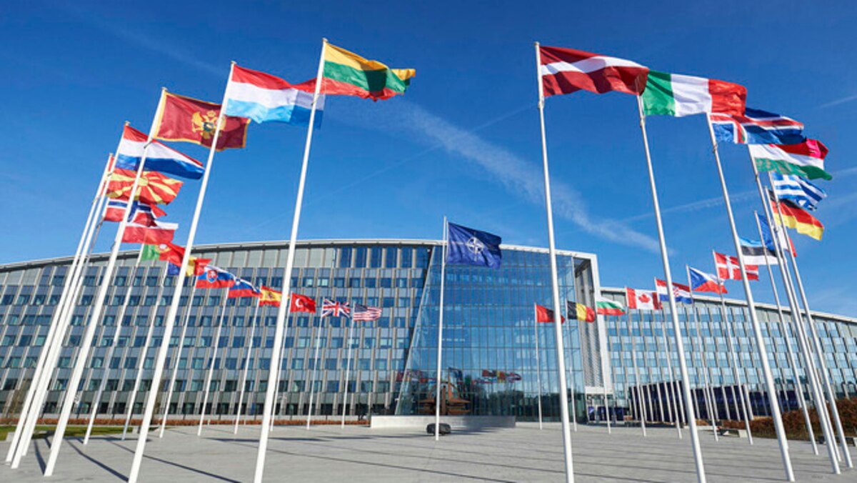 Circular display of national flags outside a glass building.