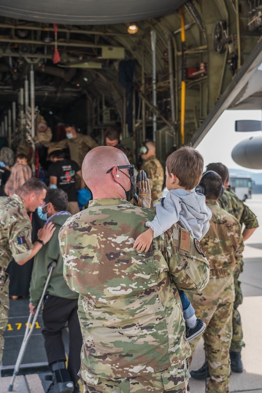 An airman carries a child onto a large military aircraft.