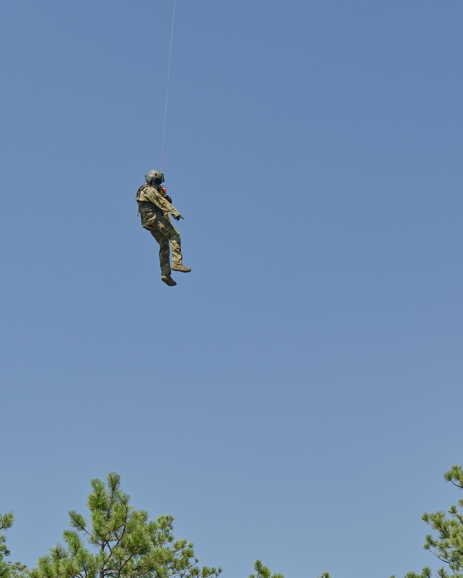 two military members hang from helicopter