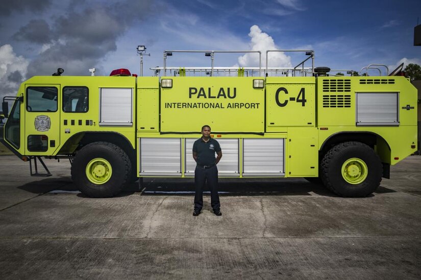 A man poses with a fire truck in the background.