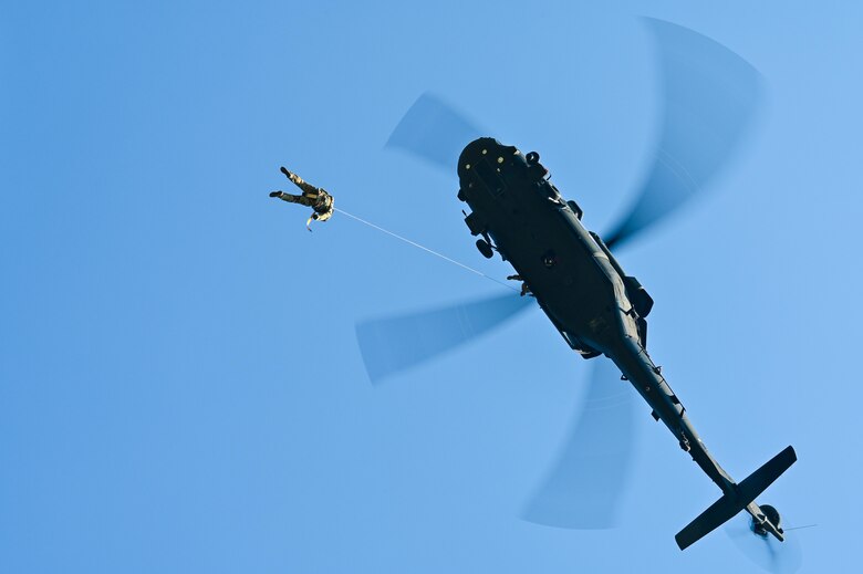 two military members hang from helicopter