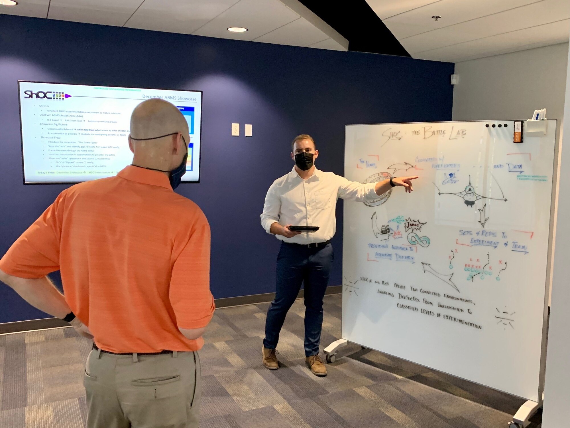 Photo of man briefing another man in front of whiteboard