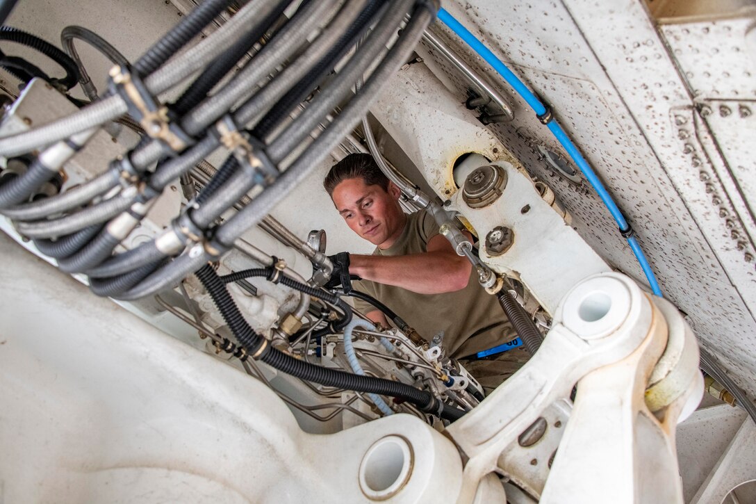 An airman wearing gloves works on a mix of hoses and pipes.
