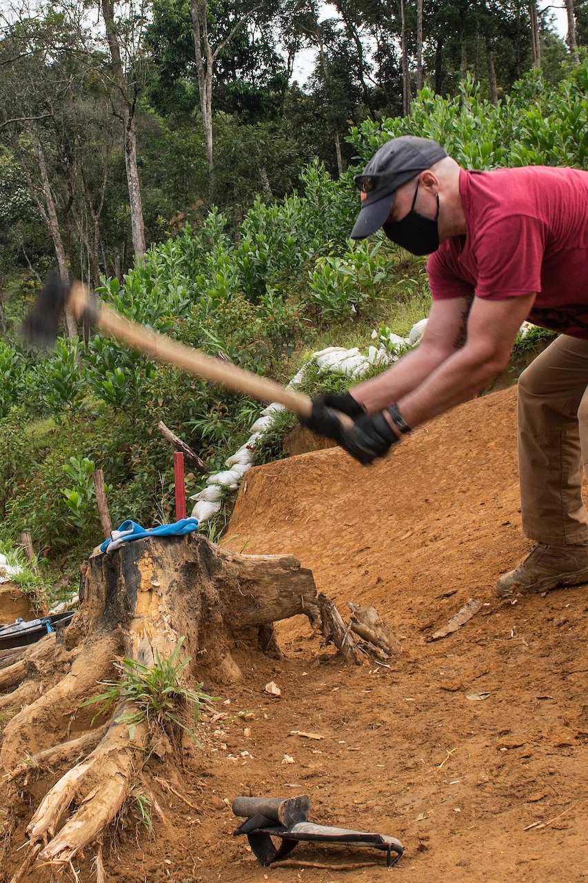 A service member uses an axe to cut a tree in the woods.