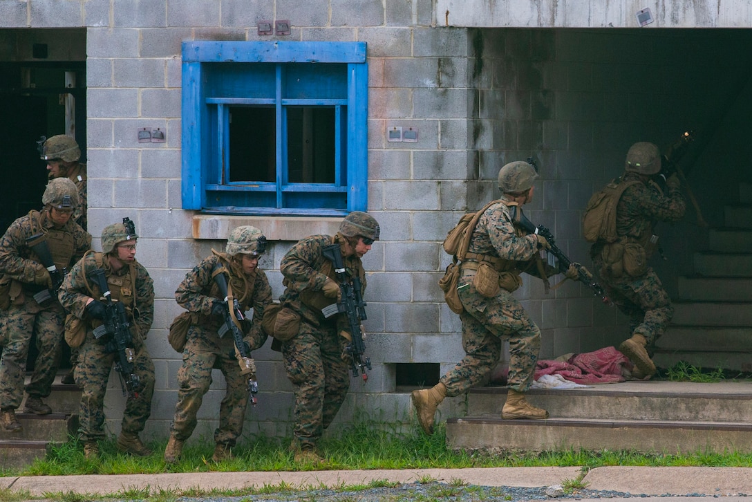 Marines run alongside a wall into a building.