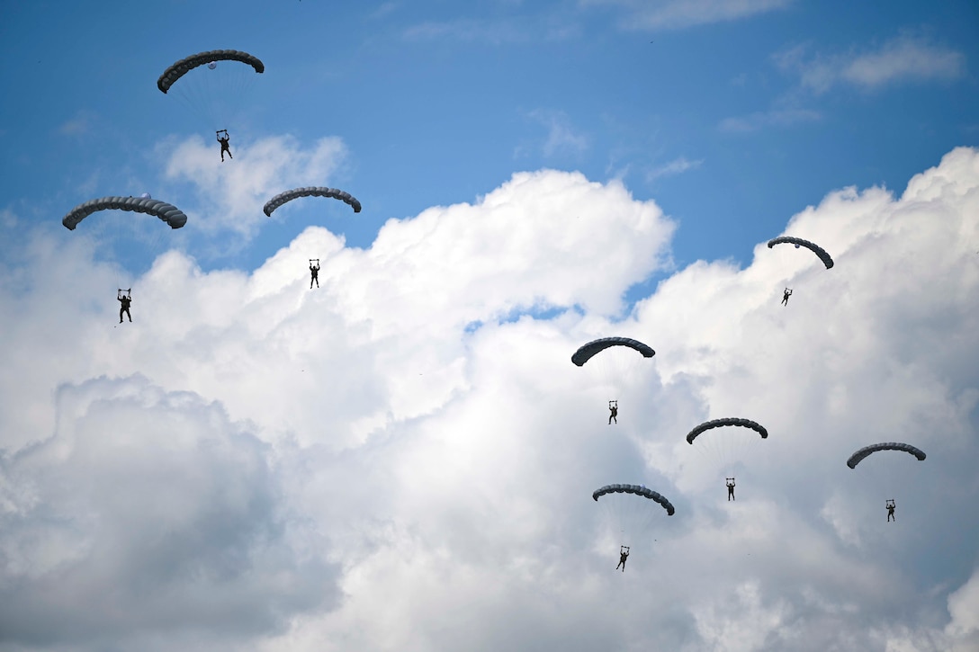 Airmen wearing parachutes descend in the sky.