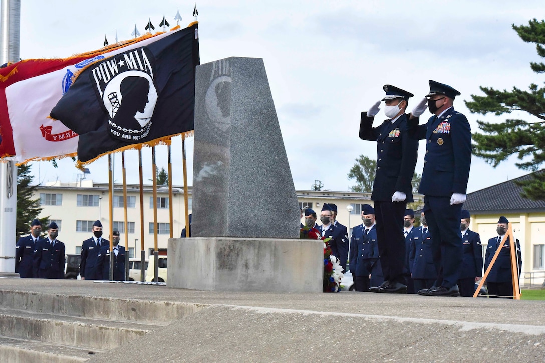 Two service members salute a monument.