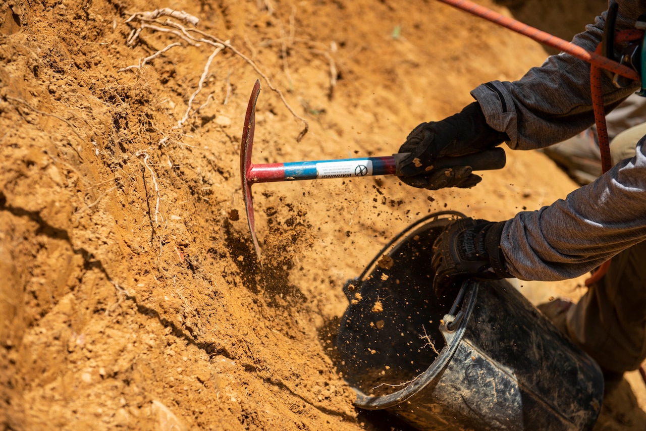 A person uses a shovel to remove dirt from the side of a mountain.