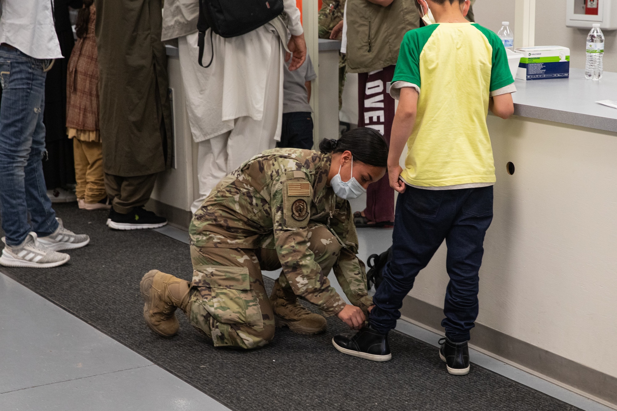 A Task Force-Holloman Airman ties an Afghan child’s shoes as he waits to in process at Holloman Air Force Base, New Mexico, Sept. 2, 2021. The Department of Defense, through U.S. Northern Command, and in support of the Department of Homeland Security, is providing transportation, temporary housing, medical screening, and general support for at least 50,000 Afghan evacuees at suitable facilities, in permanent or temporary structures, as quickly as possible. This initiative provides Afghan personnel essential support at secure locations outside Afghanistan. (U.S. Army photo by Spc. Nicholas Goodman)