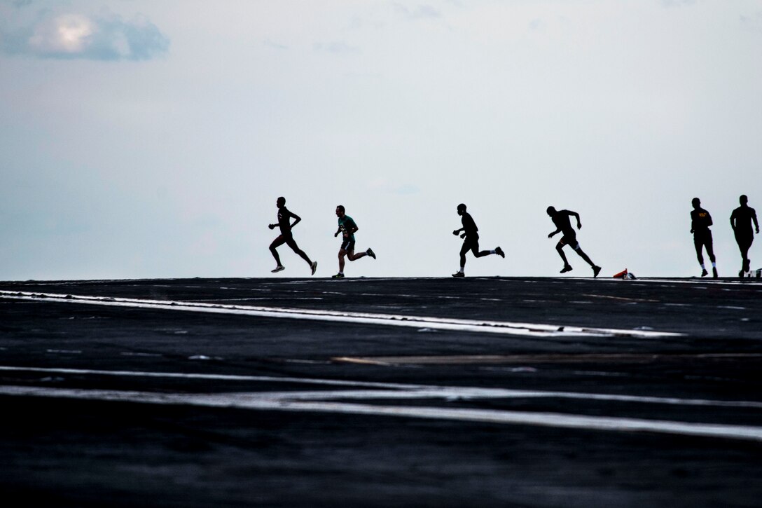 Sailors in silhouette run on a flight deck.