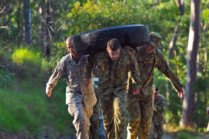 Three men in military uniforms carry a large tire.
