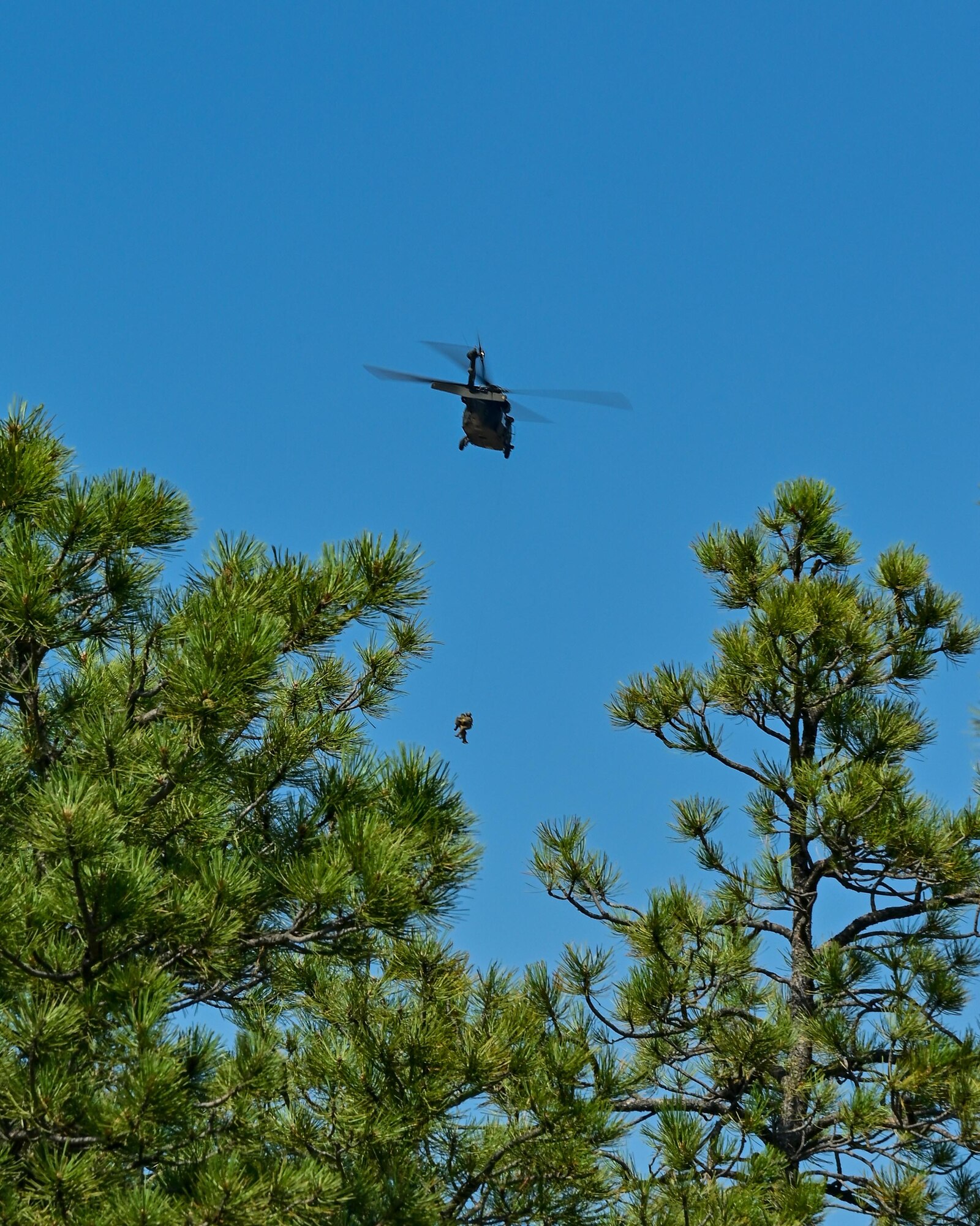 two military members hang from helicopter