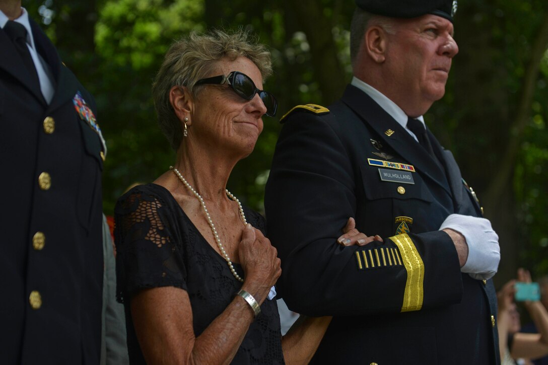 A woman puts her hand over her heart while holding onto the arm of a service member.