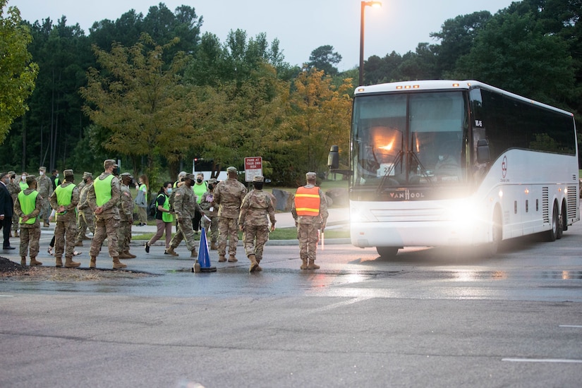 Soldiers stand in a parking lot as a bus pulls up.