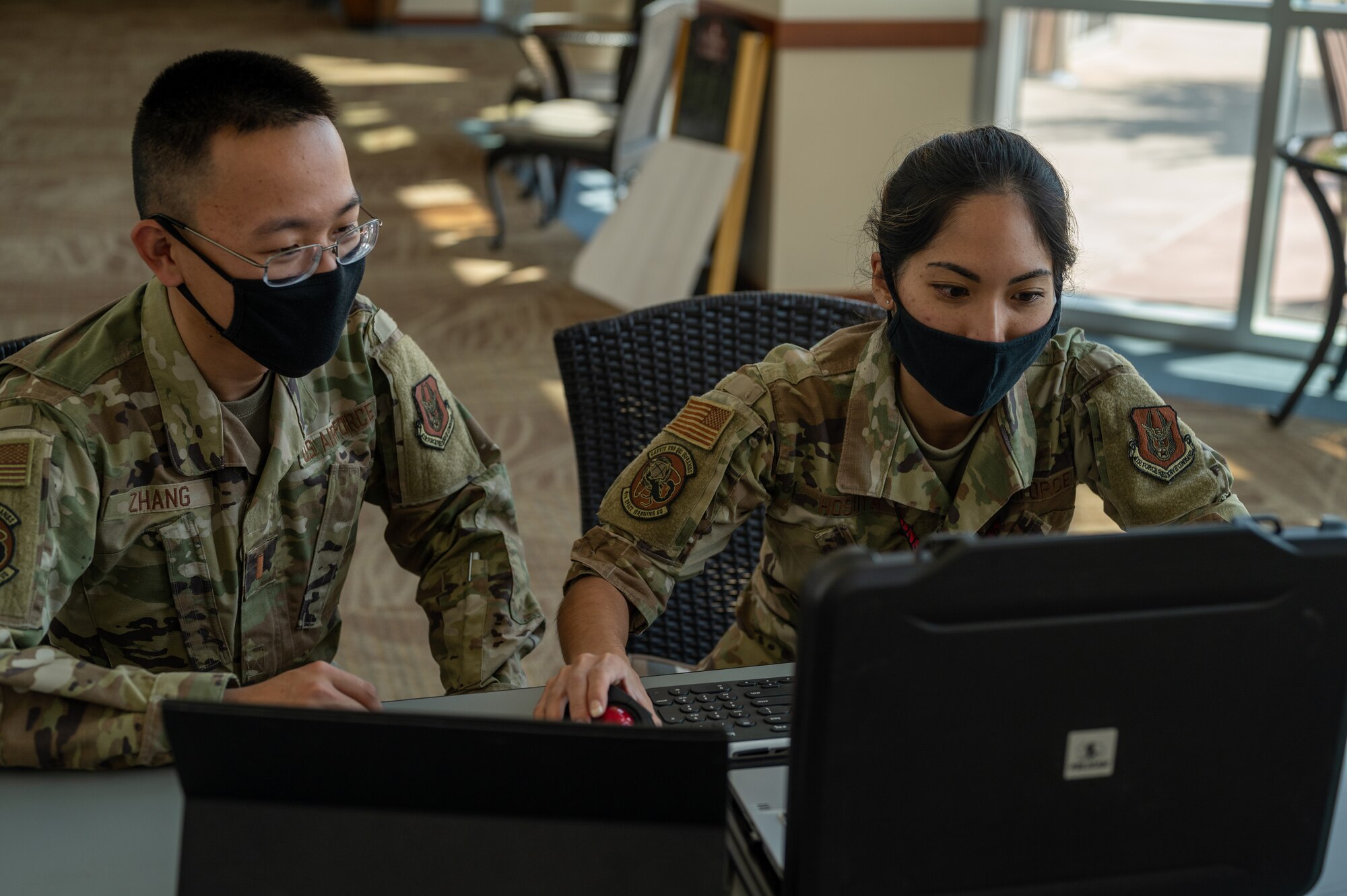 Photo of a man and a woman wearing facemasks looking at a pair of laptops.