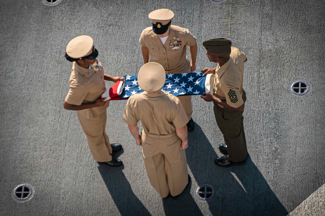 A Marine and three sailors fold an American Flag.