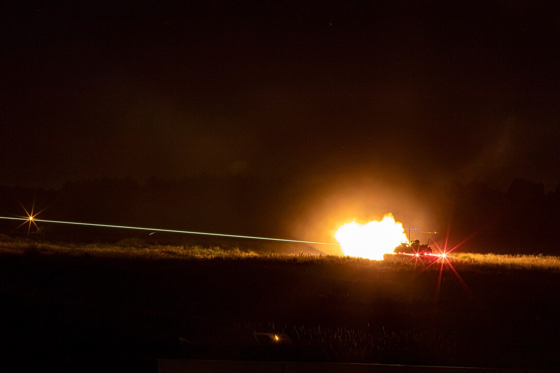 A soldier fires a weapon in a field in the dark.