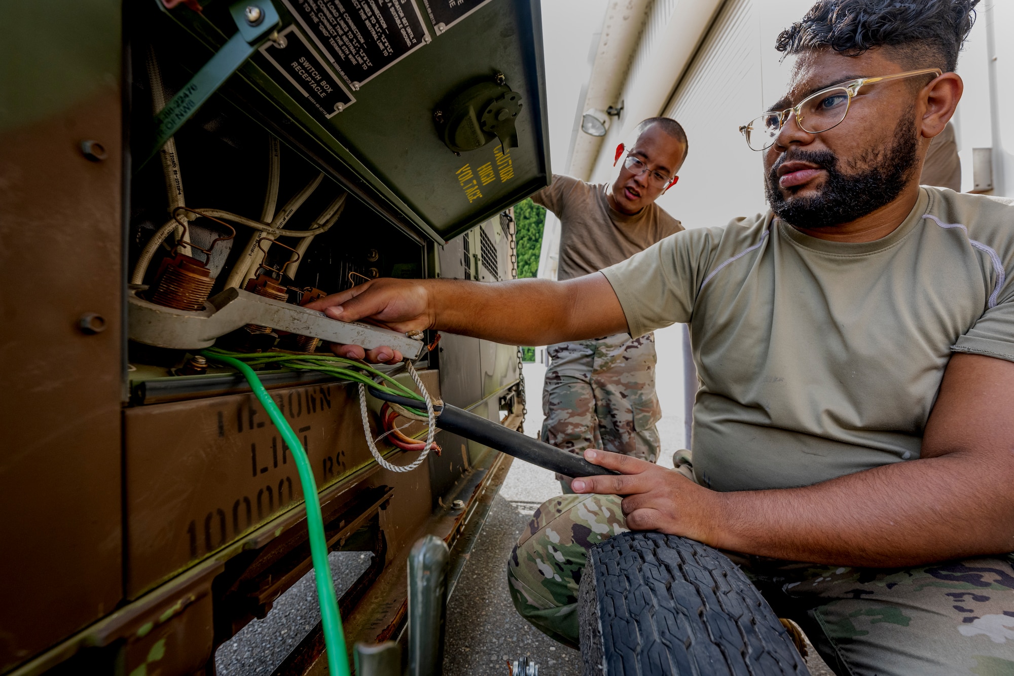 A man in uniform uses a wrench-like tool to connect large wires to a piece of machinery.