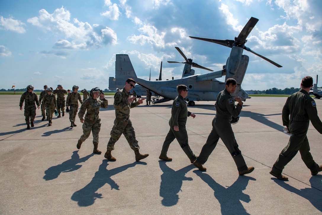 A line of service members walk from an aircraft on a flightline.