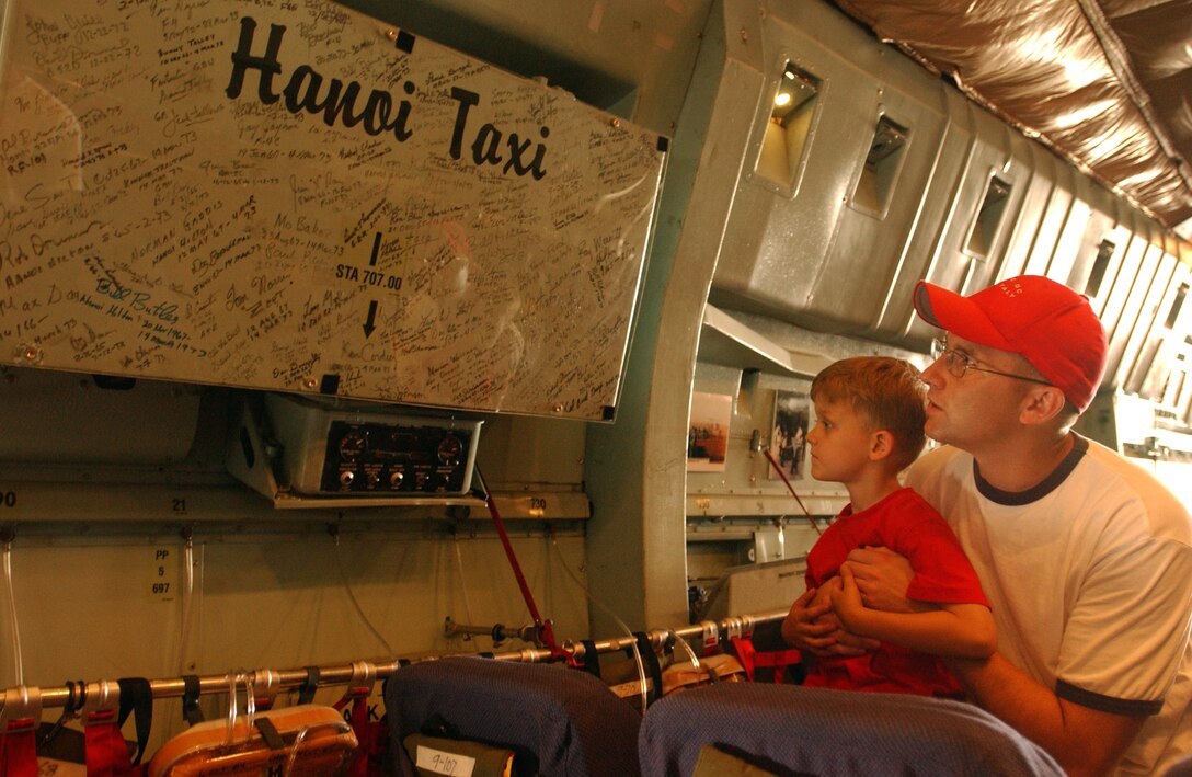 A man and child looking at the wall of signatures aboard the C-141 Starlifter known as the Hanoi Taxi