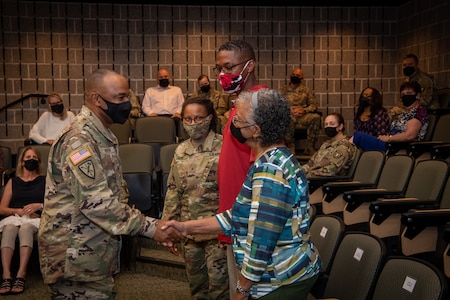 a man in uniform shakes the hands of a group of 3 people.