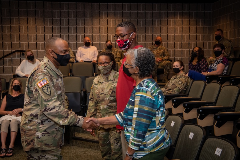 a man in uniform shakes the hands of a group of 3 people.