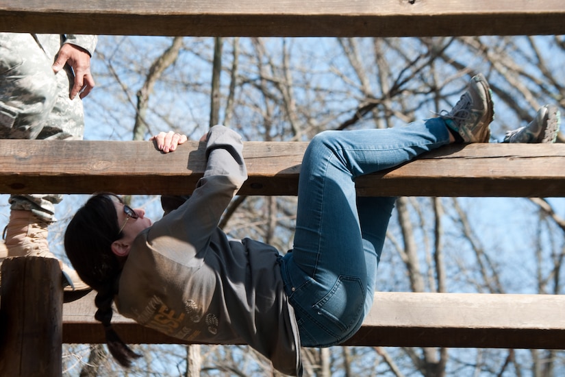 A woman hangs from a wooden bar.