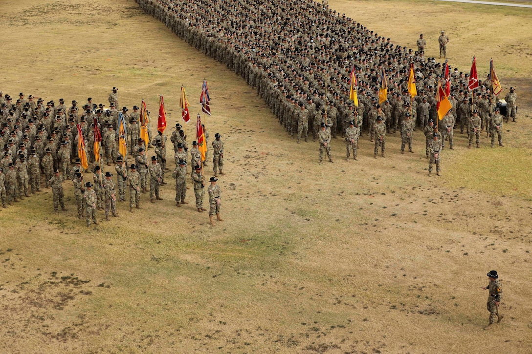 Soldiers gather in a field, some holding flags.