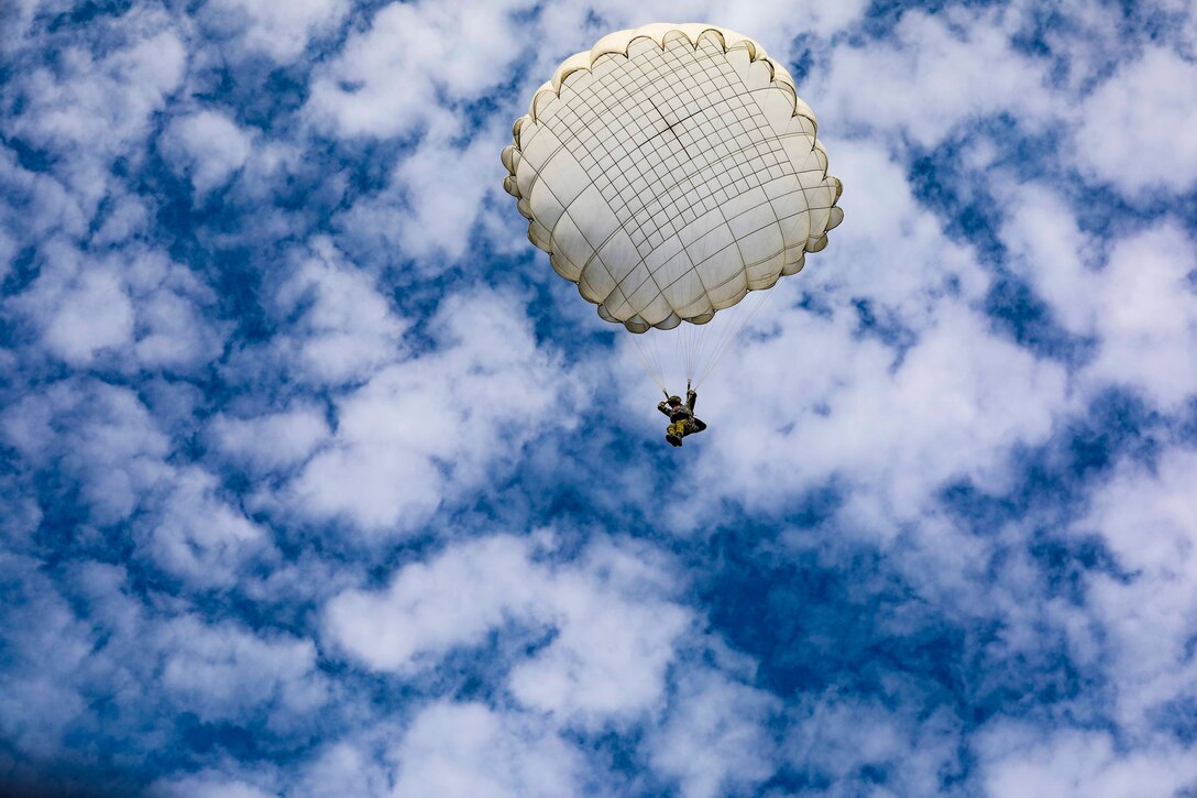 A soldier descends in the sky wearing a parachute.