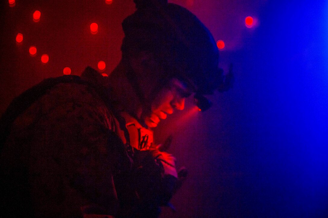 A Marine looks down while illuminated by red and blue light.