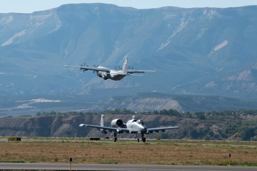 One airplane lands as another takes off with mountains in the background.