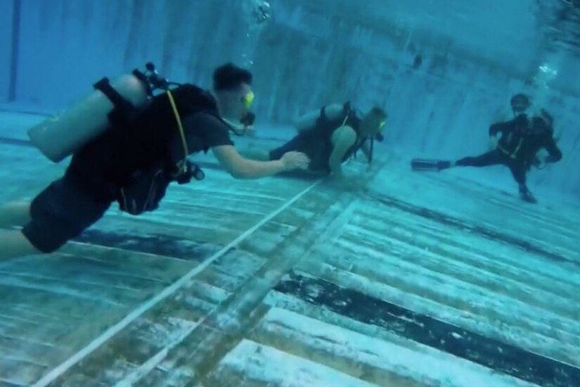 Three people scuba dive in a pool.