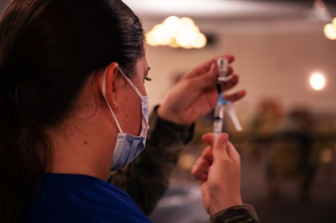 An airman wearing a face mask inserts a syringe into a small bottle.