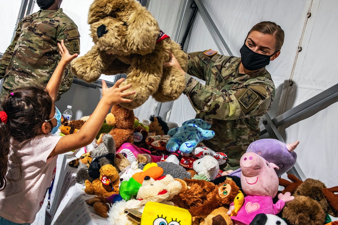 A soldier hands a stuffed animal over a pile to a child.