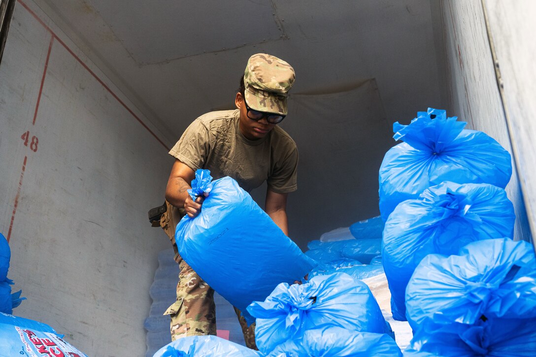 A soldier unpacks blue bags filled with ice in the back of a truck.