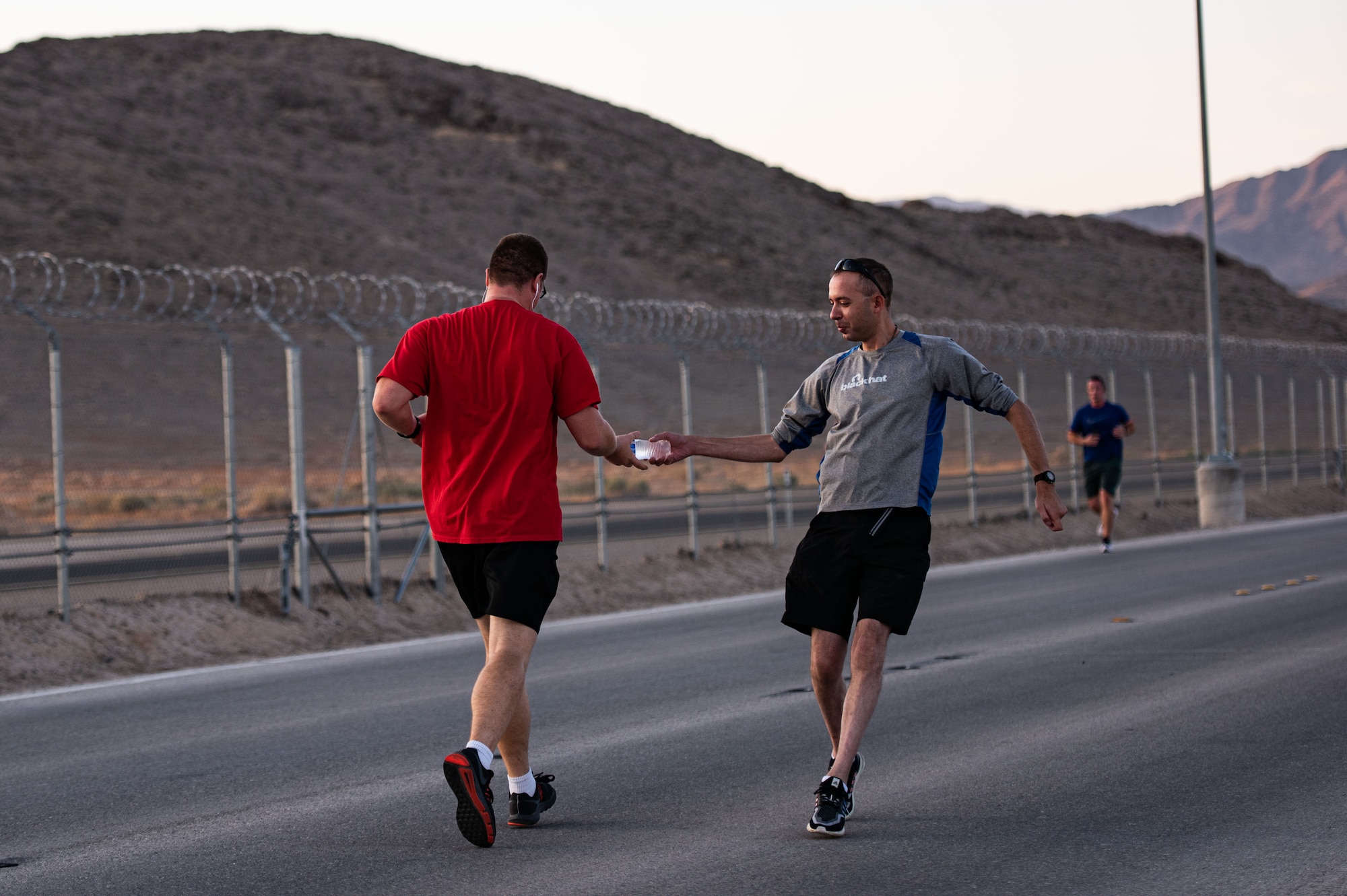 An airman gives a runner a water bottle as he runs past.
