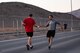 An airman gives a runner a water bottle as he runs past.