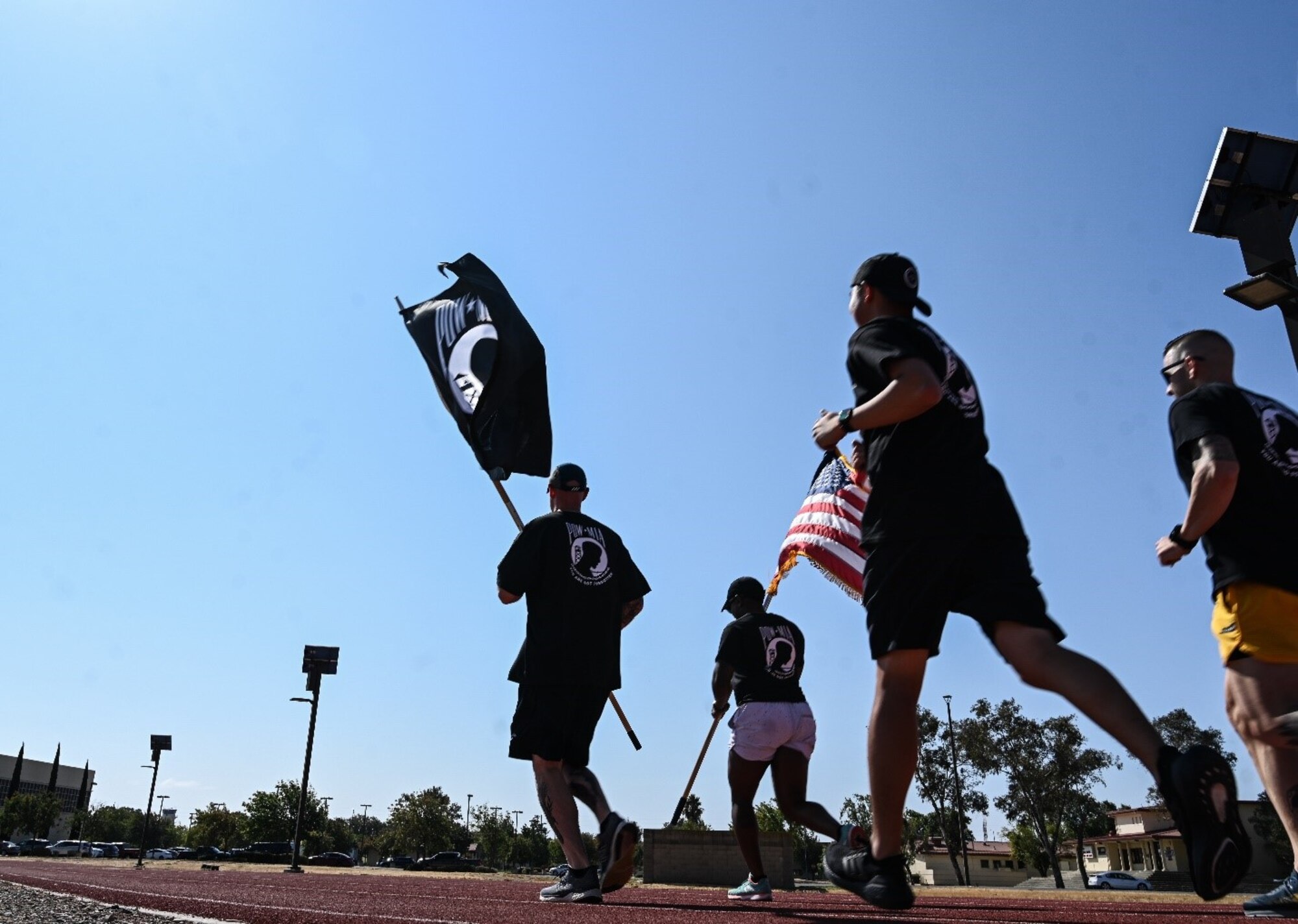 People in fitness attire run with the POW/MIA and U.S. flag on a  sunny day