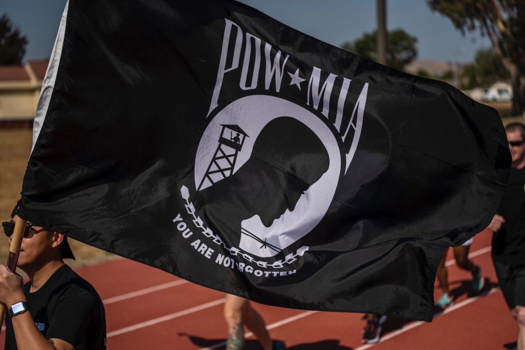 A man in a black shirt carries the POW/MIA flag while running on a sunny day