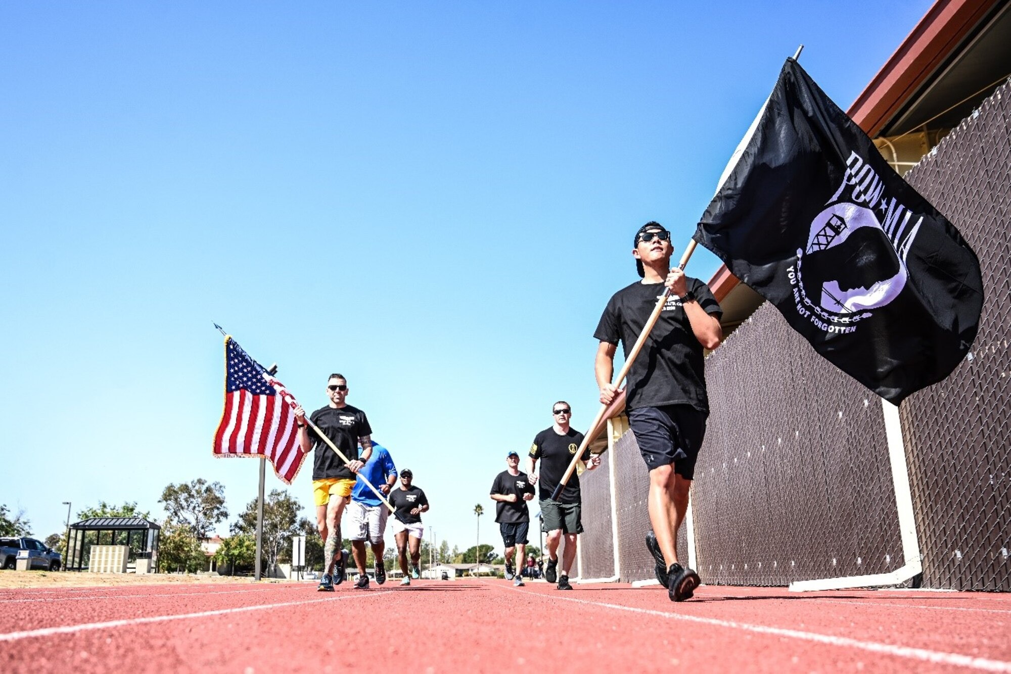 People in fitness attire run with the U.S. and POW/MIA flags on a sunny day