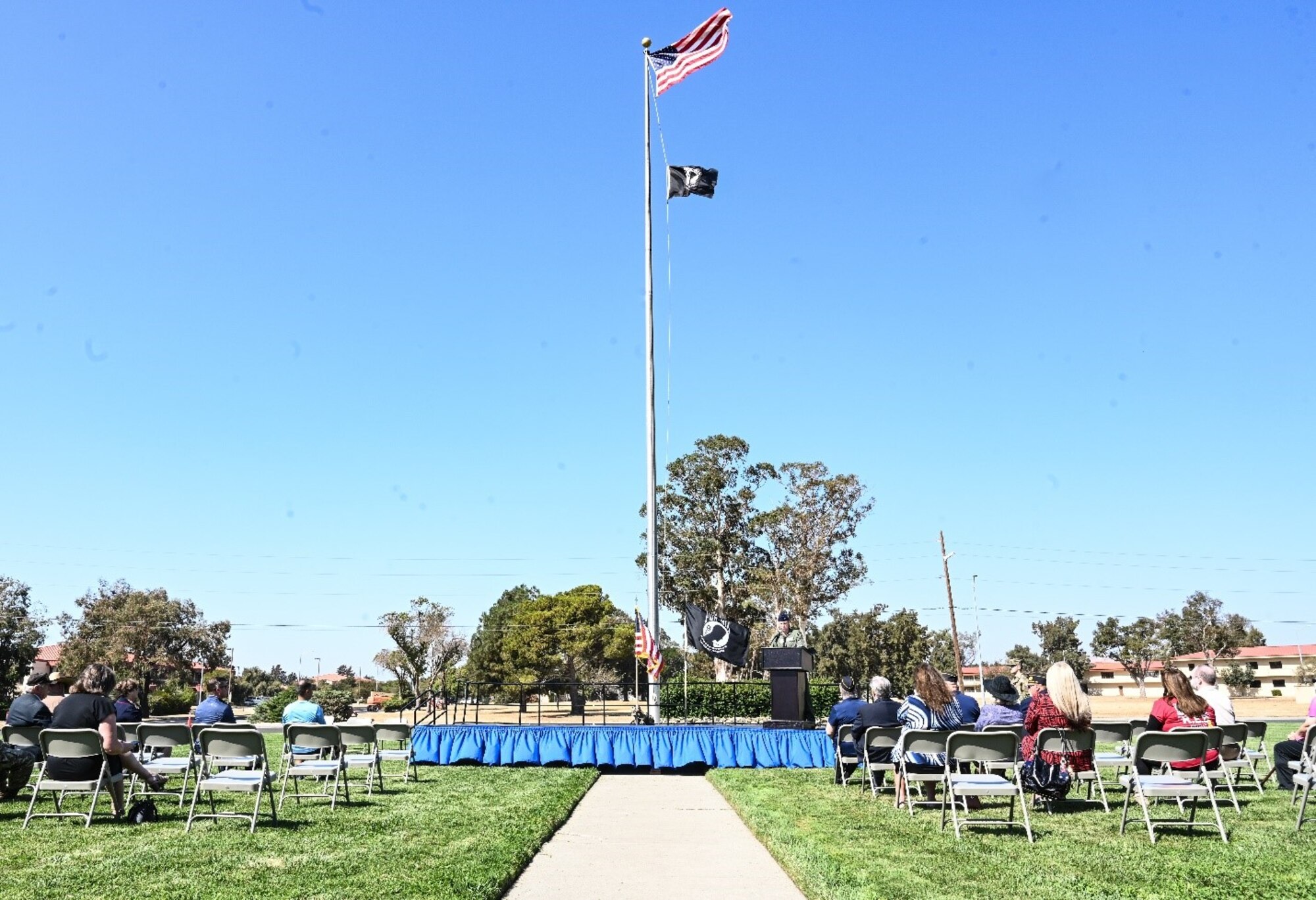 A stage is at the center of a congregation of attendees with a flag pole featured prominently on a sunny day