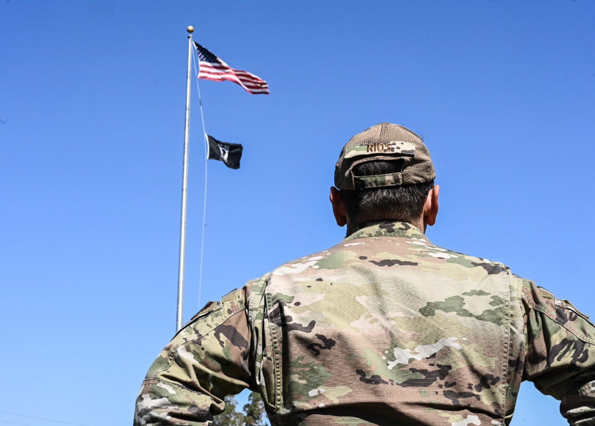 A uniformed Airman looks up at a flag pole bearing the U.S. and POW/MIA flags