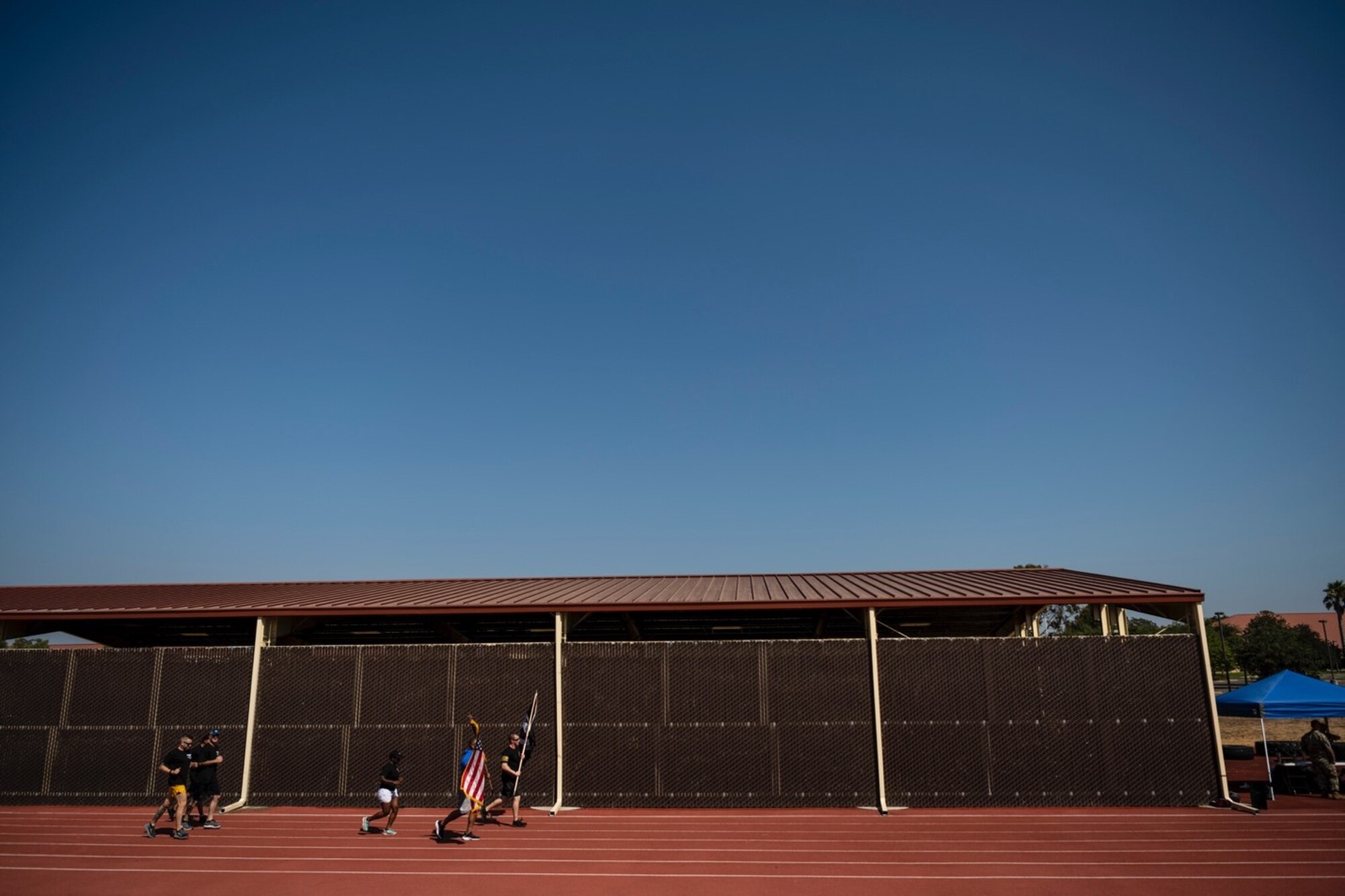 People in fitness attire run while carrying the U.S. and POW/MIA flag on a sunny day
