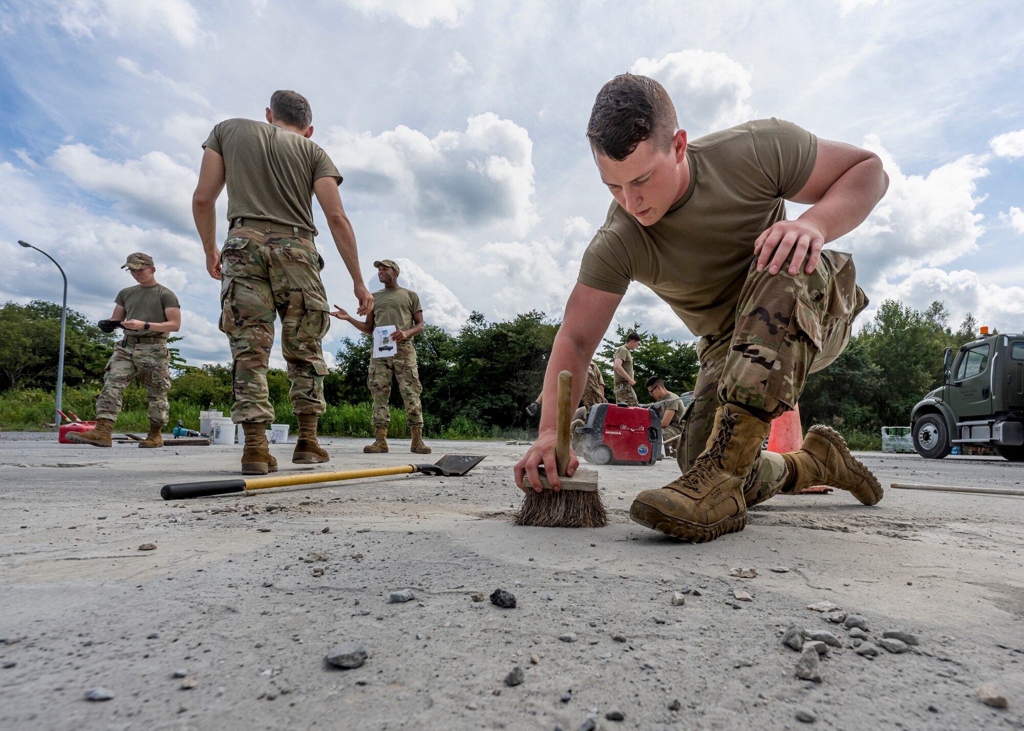 A man in uniform uses a brush to clean out a divot in concrete.