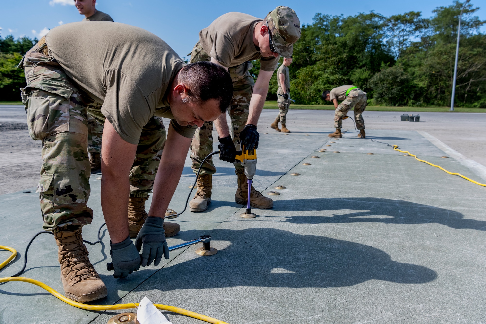 People in uniform use power tools to attach a surface to the ground.