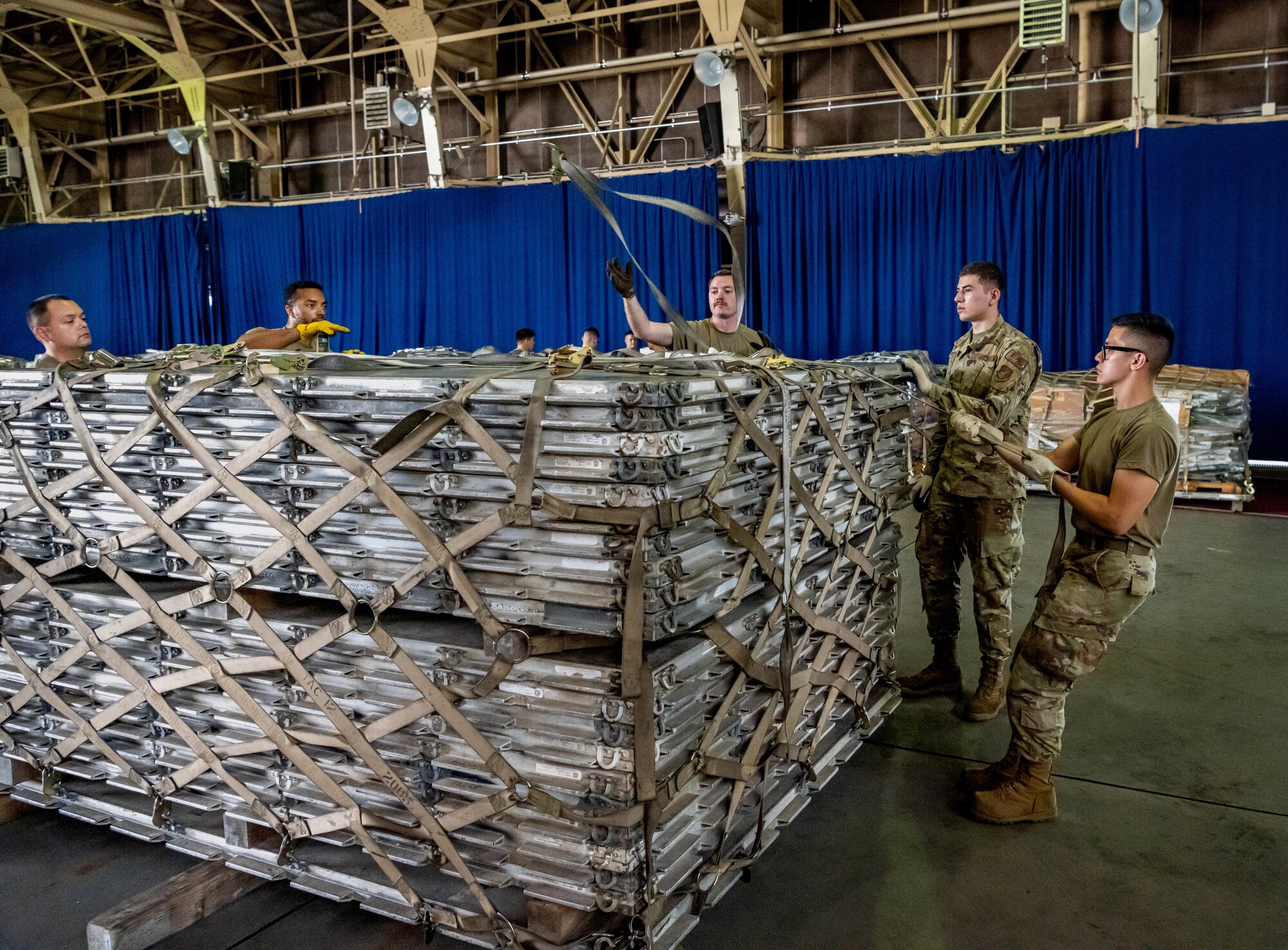 People pull on heavy duty ratchet straps to secure a large piece of cargo.